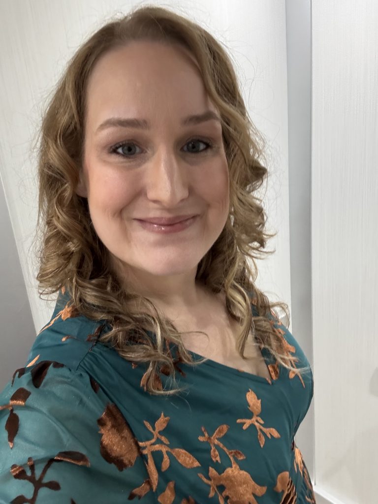 A Selfie of Renee Yarrington. She has curly, shoulder-length, blonde hair and is wearing a blue blouse with a floral print. She is smiling slightly, in a way that says she is pleased to meet you.